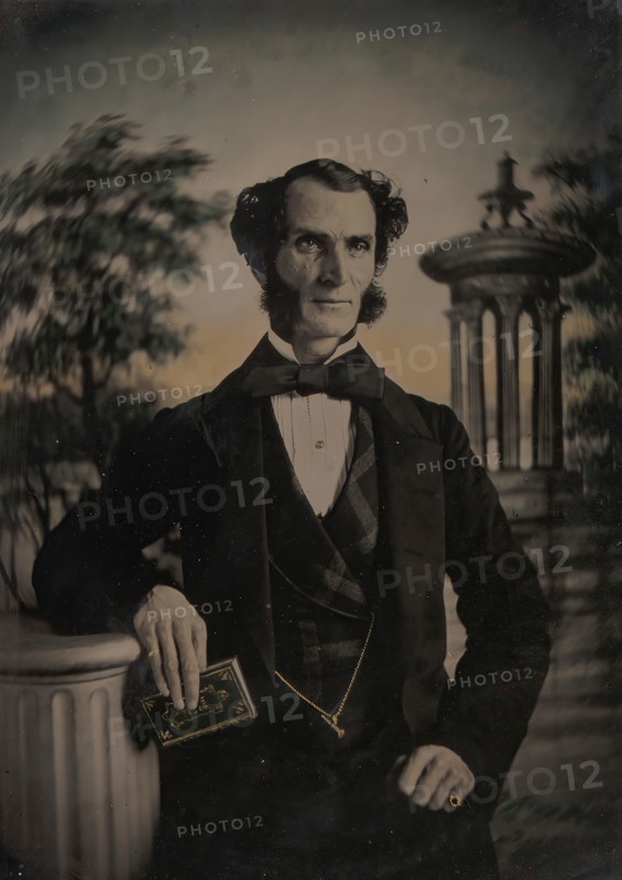 Man Holding Book, Standing Before a Painted Scenic Backdrop, 1850s-60s.