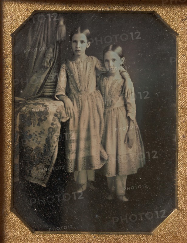 Two Identically Dressed Young Girls Standing Next to a Table, 1840s.