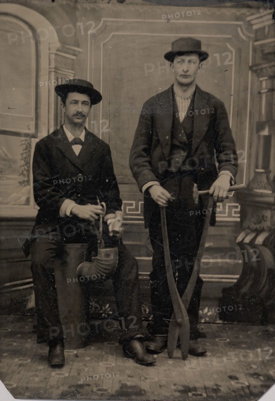 Two Stovepipe Makers, One with a Hammer and Tin Snips, the Other Sitting on Stovepipe Assembly with Tin Snips and Mallet, 1880s.