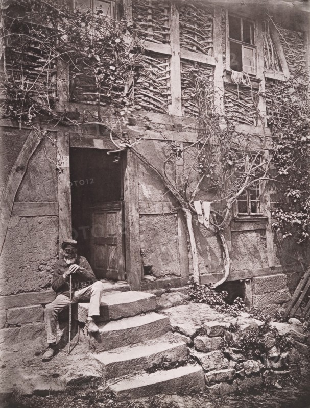 [Man Sitting on Steps of House with Socks Hanging on Nearby Vine to Dry], 1880s.