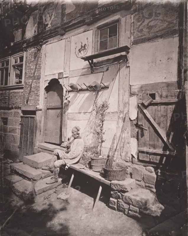 [Man Smoking Pipe Outside His Home on Village Street], 1880s.