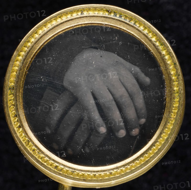 Two hands resting on a book set into a two-piece gold-washed brass frame