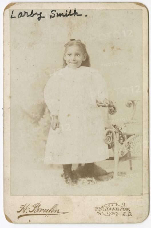 Photograph of Larby Smith standing next to a wicker chair., late 19th century. Creator: Henry Bruhn.