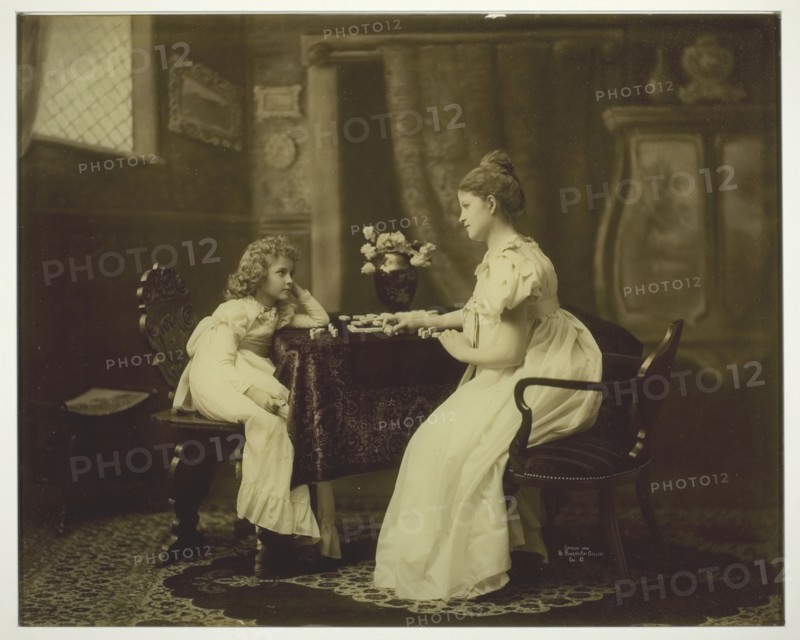 Woman and Child Playing Dominoes at Table, c. 1898. Creator: Unknown.