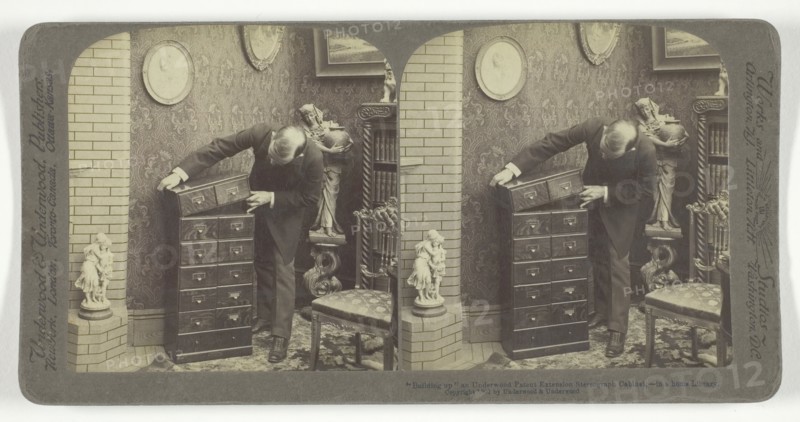 Building up an Underwood Patent Extension Stereograph Cabinet, - in a home Library, 1901. Creator: Underwood & Underwood.