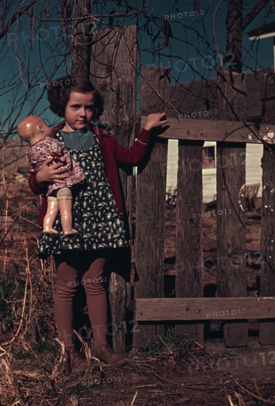 Girl with doll standing by fence, between 1941 and 1942. Creator: Unknown.