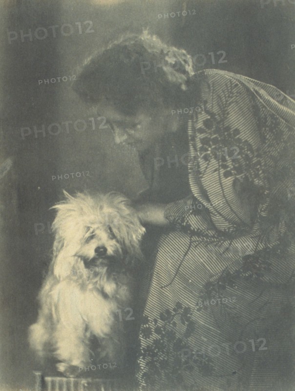 Seated woman petting her white dog, c1900.
