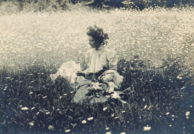Woman with wreath of leaves in her hair sitting in a field of daisies, c1900. Creator: Unknown.