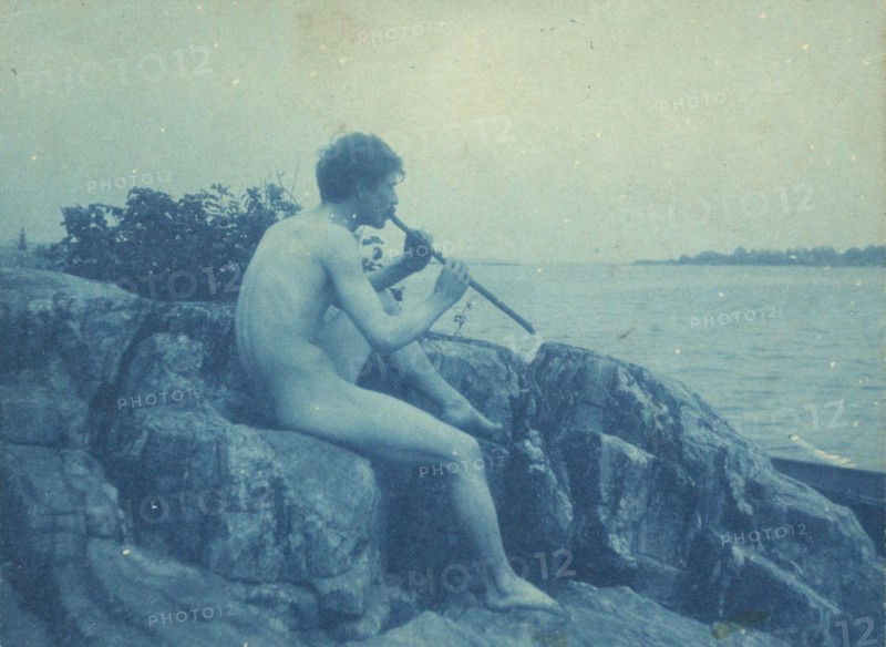 Man posed on rocks, nude, playing pipe (Pan), between 1885 and 1900.