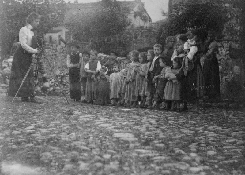 Frances Benjamin Johnston photographing a group of people, mostly children, in Europe, 1900.