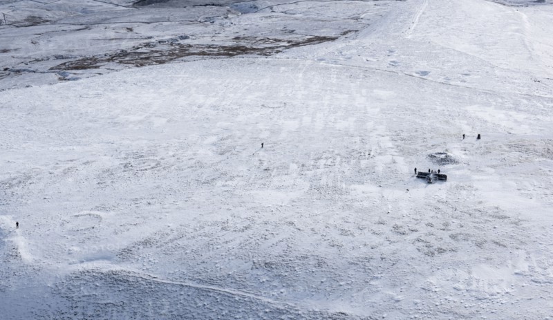 Walkers on a snowy Ingleborough Hillfort, with hut circle earthworks also visible, North Yorkshire, 2018.