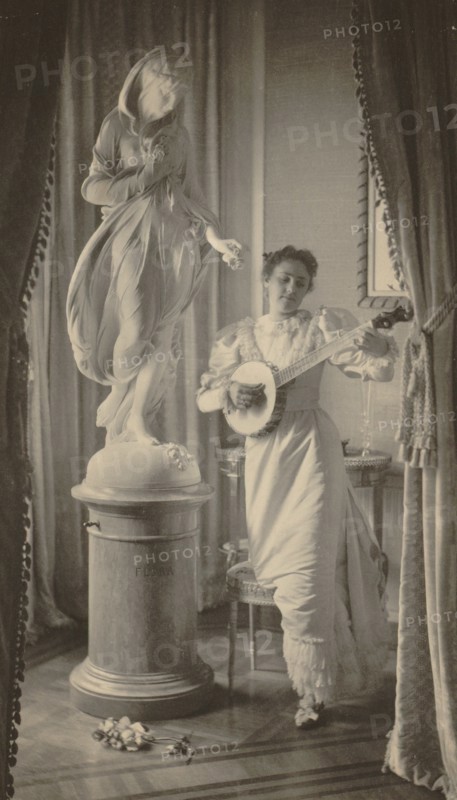 Miss Apperson playing banjo beside statue of "Flora" in niche of Sen. George Hearst's residence, Washington, D.C., 1895.