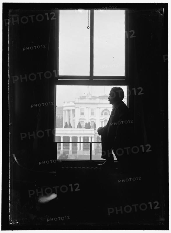 John Skelton Williams at window with White House visible in background, Washington, D.C.