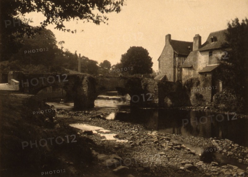 View of a stone bridge, river and buildings in a village, probably in France , c1890.