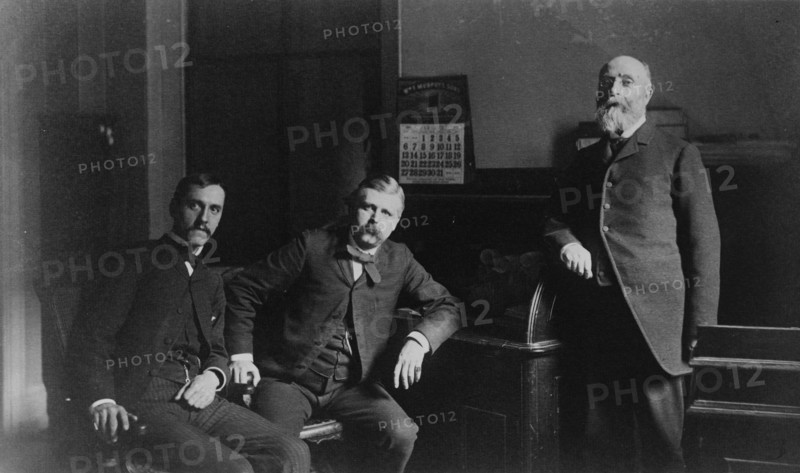 Three Treasury Department employees, Mr. Steele(?) and two other men, posed in office, between 1884 and 1930.