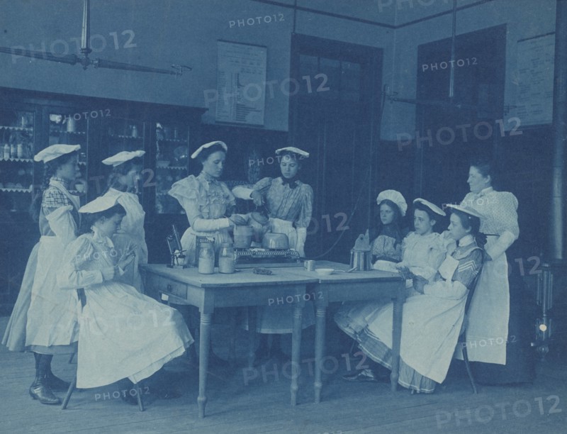 Eight teenage girls wearing aprons and chef caps learning to cook...Washington DC high school, 1899? Creator: Frances Benjamin Johnston.
