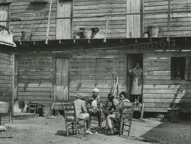 African American woman standing in doorway and African American girls sitting around..., Feb 1941. Creators: Farm Security Administration, Marion Post Wolcott.