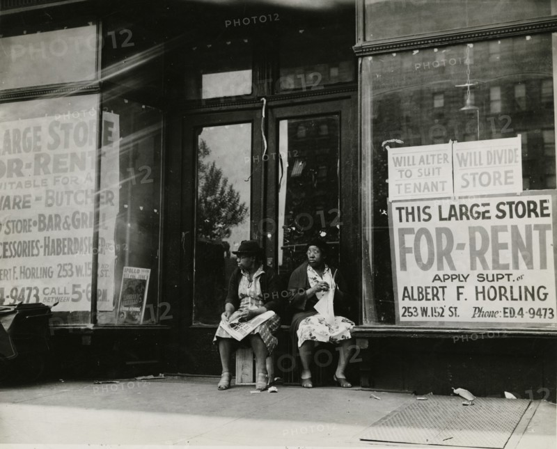 Sidewalk sitters. Two women sitting in doorway of empty storefront that is being..., ca. 1930s. Creator: Unknown.