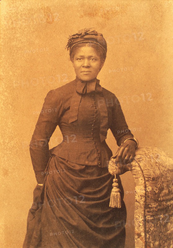 Studio portrait of woman wearing hat and gloves and dress with bustle, c1875. Creator: Unknown.