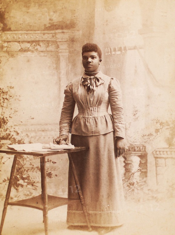Studio portrait of woman, hand on books spread on table, (1880-1940?). Creator: Madison Art Studio.
