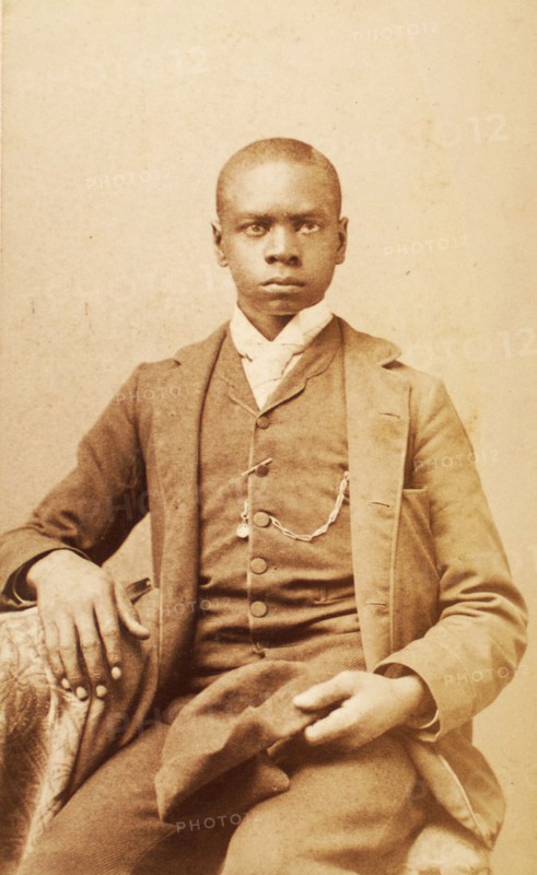 Studio portrait of unidentified seated young man, holding cap, c1880-c1889 . Creator: A. H. Plecker.