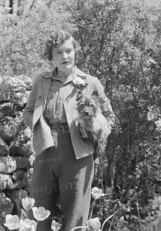 DeLamar, Alice, Miss, with dog, standing outdoors, between 1927 and 1942. Creator: Arnold Genthe.