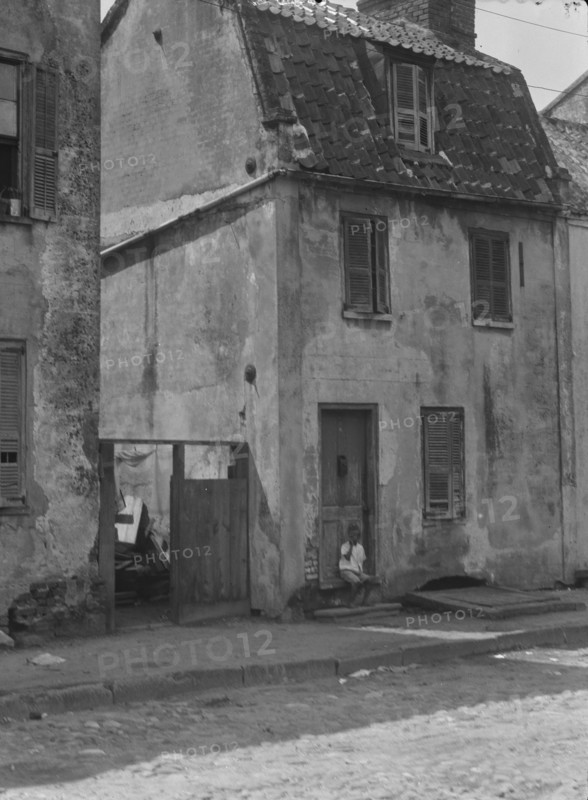 Boy sitting in the doorway of a two-story building, [17 Chalmers Street], Charleston..., c1920-c1926 Creator: Arnold Genthe.