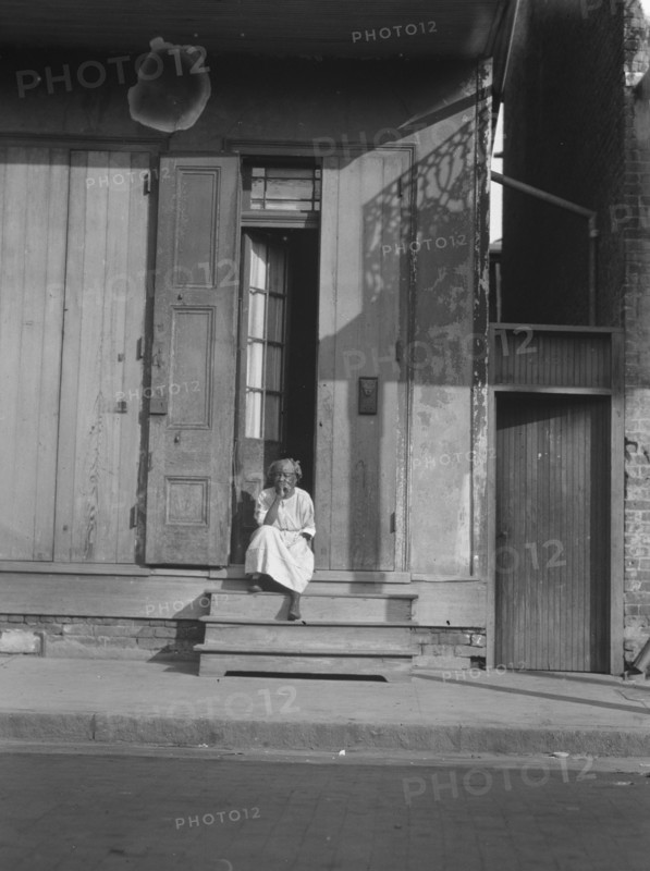 View from across street of a woman sitting on steps, New Orleans, between 1920 and 1926. Creator: Arnold Genthe.