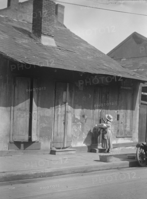 Woman holding a sack standing by the doorway of a building in the French Quarter..., c1920-c1926. Creator: Arnold Genthe.