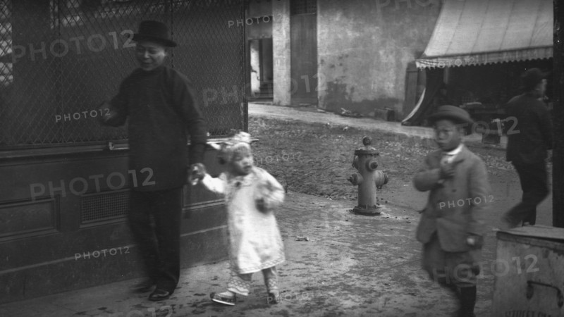 Man and a young child walking down a street, Chinatown, San Francisco, between 1896 and 1906. Creator: Arnold Genthe.