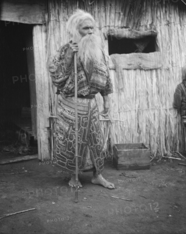Ainu man holding a staff standing outside a hut, 1908. Creator: Arnold Genthe.