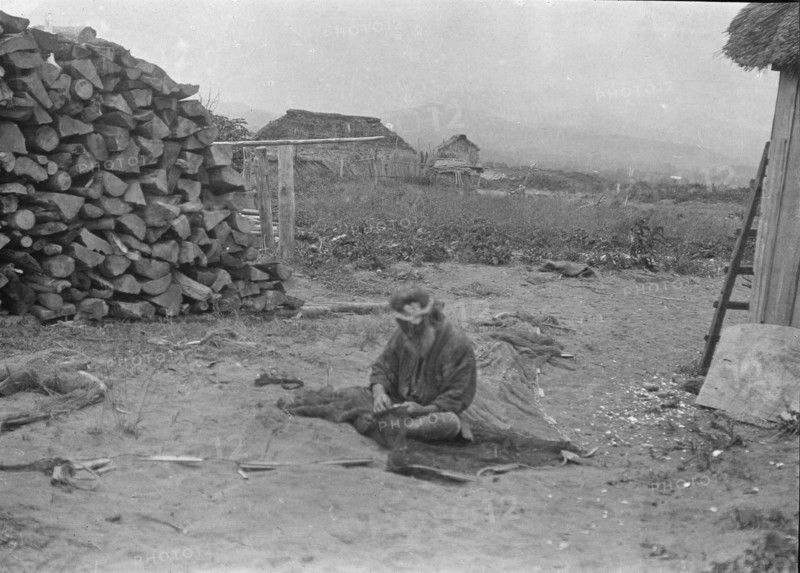 Ainu man seated outside working on nets, 1908. Creator: Arnold Genthe.