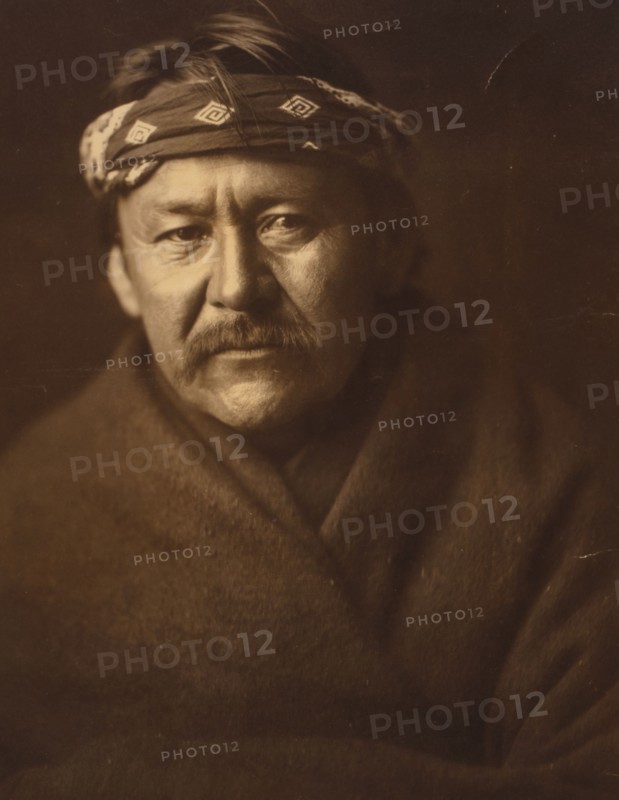 A Navajo man, head-and-shoulders portrait, wearing blanket and headband, facing front, c1904. Creator: Edward Sheriff Curtis.