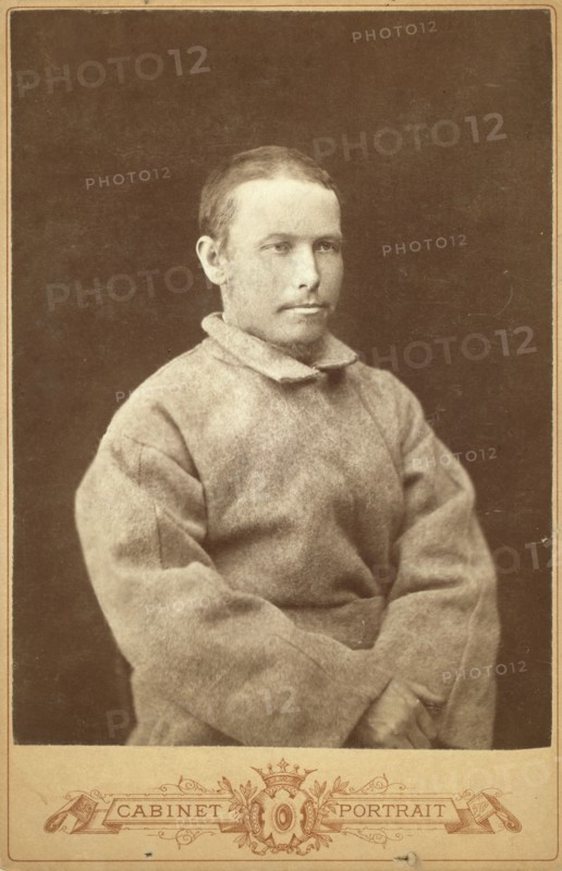 Half-length portrait of a man in convict coat, seated, facing right, between 1880 and 1886. Creator: Unknown.