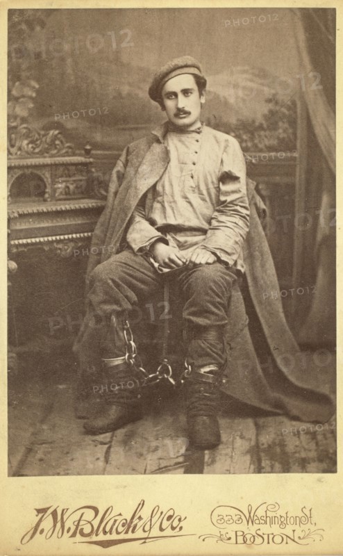 Full-length portrait of a man in convict clothing and leg irons, seated..., between 1880 and 1886. Creator: Unknown.