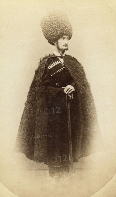 Full-length portrait of a man in cape and sheep skin hat, holding a rifle..., between 1870 and 86. Creator: Unknown.