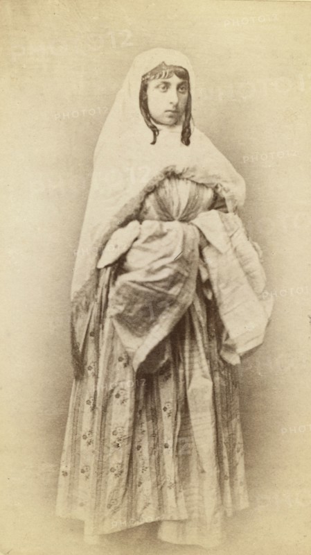 Full-length portrait of a woman, facing slightly right, in traditional dress, between 1870 and 1886. Creator: Unknown.