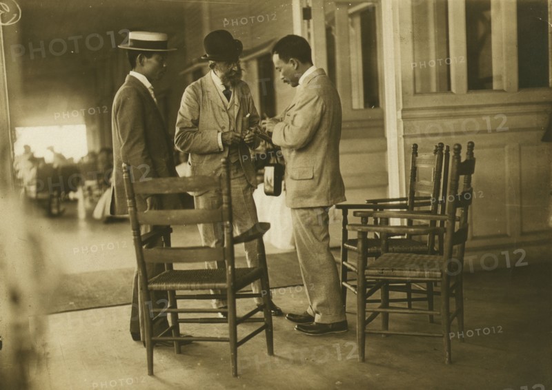 Two Japanese men and one American(?) man, probably journalists, conversing on the veranda..., 1905. Creator: Unknown.