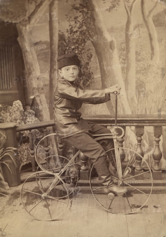A boy on a bicycle in a photo studio, 1880. Creator: Unknown.