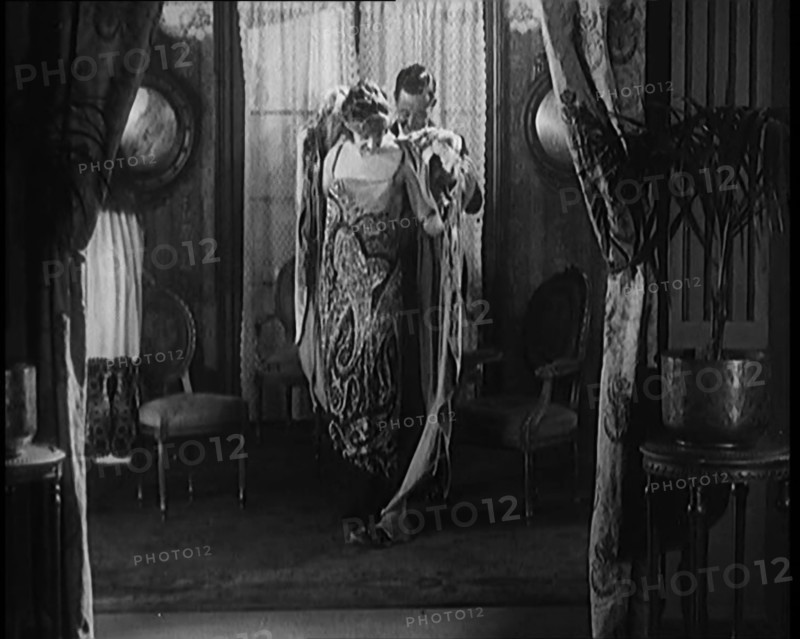 A Male Civilian Helping a Female Civilian Remove Her Fur Coat Revealing an Ornated Gown, 1920. Creator: British Pathe Ltd.