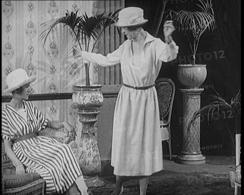 Two Female Civilians Leisuring in a Drawing Room Wearing Long Dresses and Hats Comparing..., 1920. Creator: British Pathe Ltd.