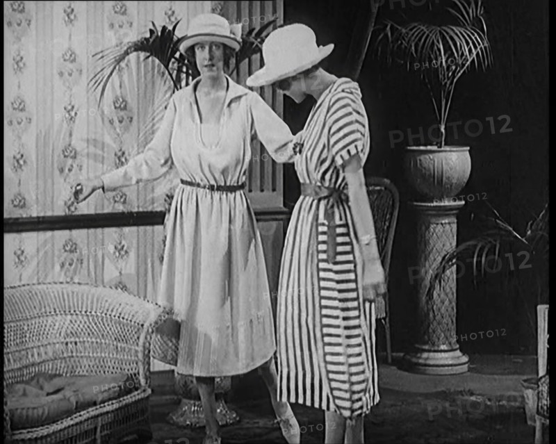 Two Female Civilians Leisuring in a Drawing Room Wearing Long Dresses and Hats Comparing..., 1920. Creator: British Pathe Ltd.