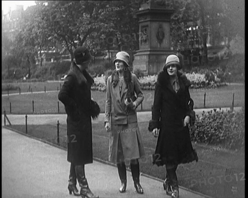 Three Female Civilians Wearing Glamorous Outfits and Long Boots Walking on a Park, 1920. Creator: British Pathe Ltd.