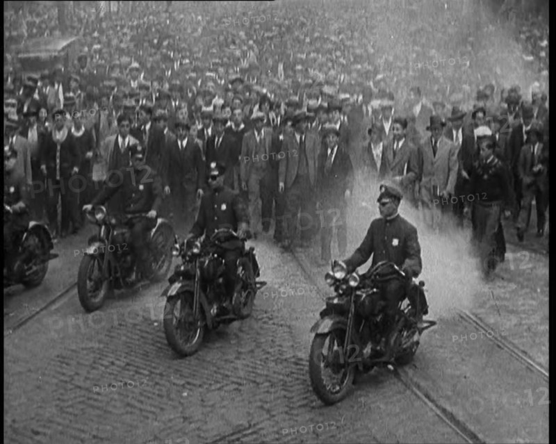 Male American Police Officers Riding Motorbikes Escorting a Large Crowd in a Parade, 1930. Creator: British Pathe Ltd.