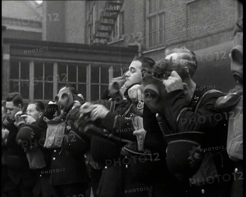 Male Police Civil Defence Volunteers Practice Putting on Gas Masks in a Yard Behind a Brick..., 1938 Creator: British Pathe Ltd.
