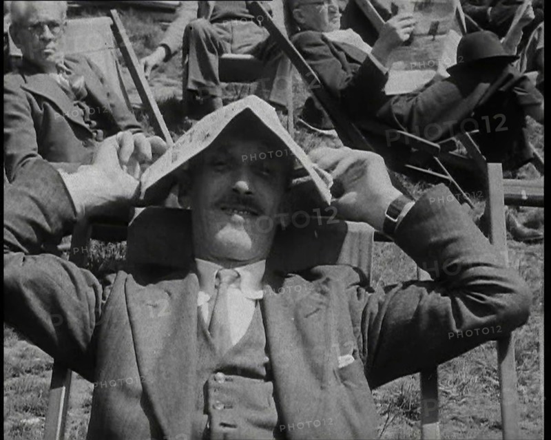 British Man in a Three Piece Suit Sitting in a Deckchair Smiling at the Camera and Holding..., 1938. Creator: British Pathe Ltd.