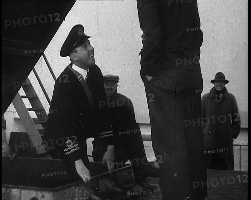 A Male Customs Official Standing by a Hatch and Talking to a Man on Board a Large Ship in..., 1939. Creator: British Pathe Ltd.