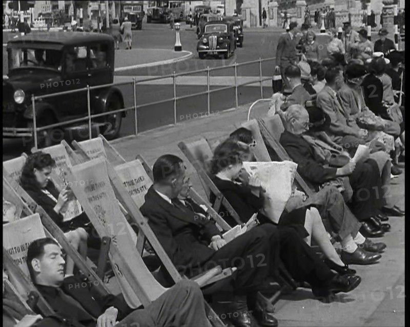 British Holidaymakers Sitting on Deckchairs on the Promenade at Brighton and Cars Driving..., 1938. Creator: British Pathe Ltd.