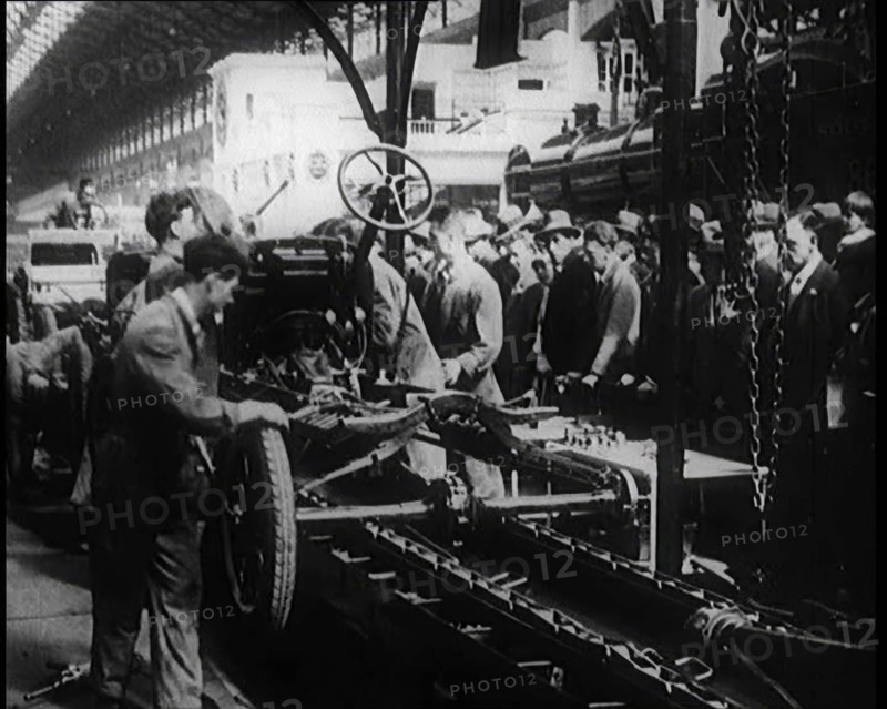 A Group of Male Civilians Building a Car As a Crowd of People Watch. Behind the Crowd..., 1924. Creator: British Pathe Ltd.