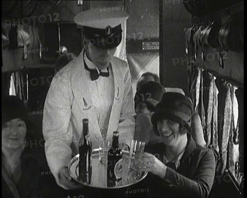 A Male Waiter Serves Smiling and Laughing Passengers Drinks  Inside an Aircraft, 1920s. Creator: British Pathe Ltd.